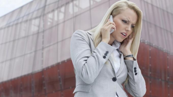 Žena s ADHD poslouchá někoho na mobilní telefon a rozhněvá se před vysokou budovou